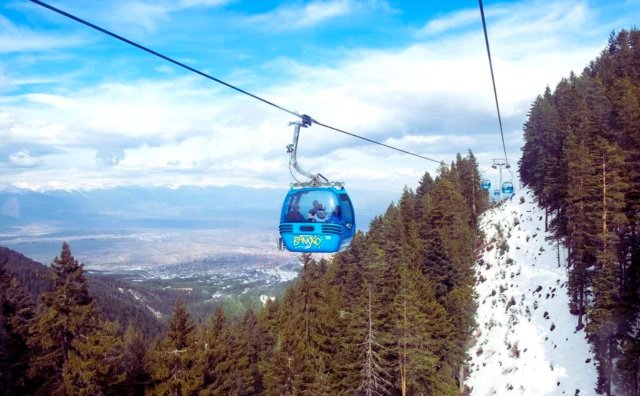 Skiers enjoy sunny spring conditions on Bansko slopes with deep snow coverage and scenic Pirin Mountains backdrop